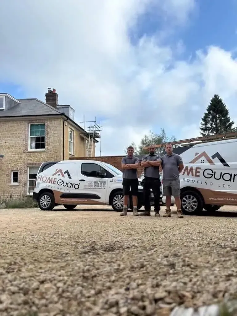 Three HomeGuard Roofing Ltd team members standing in front of two company vans at a new build or re-roofing project site.